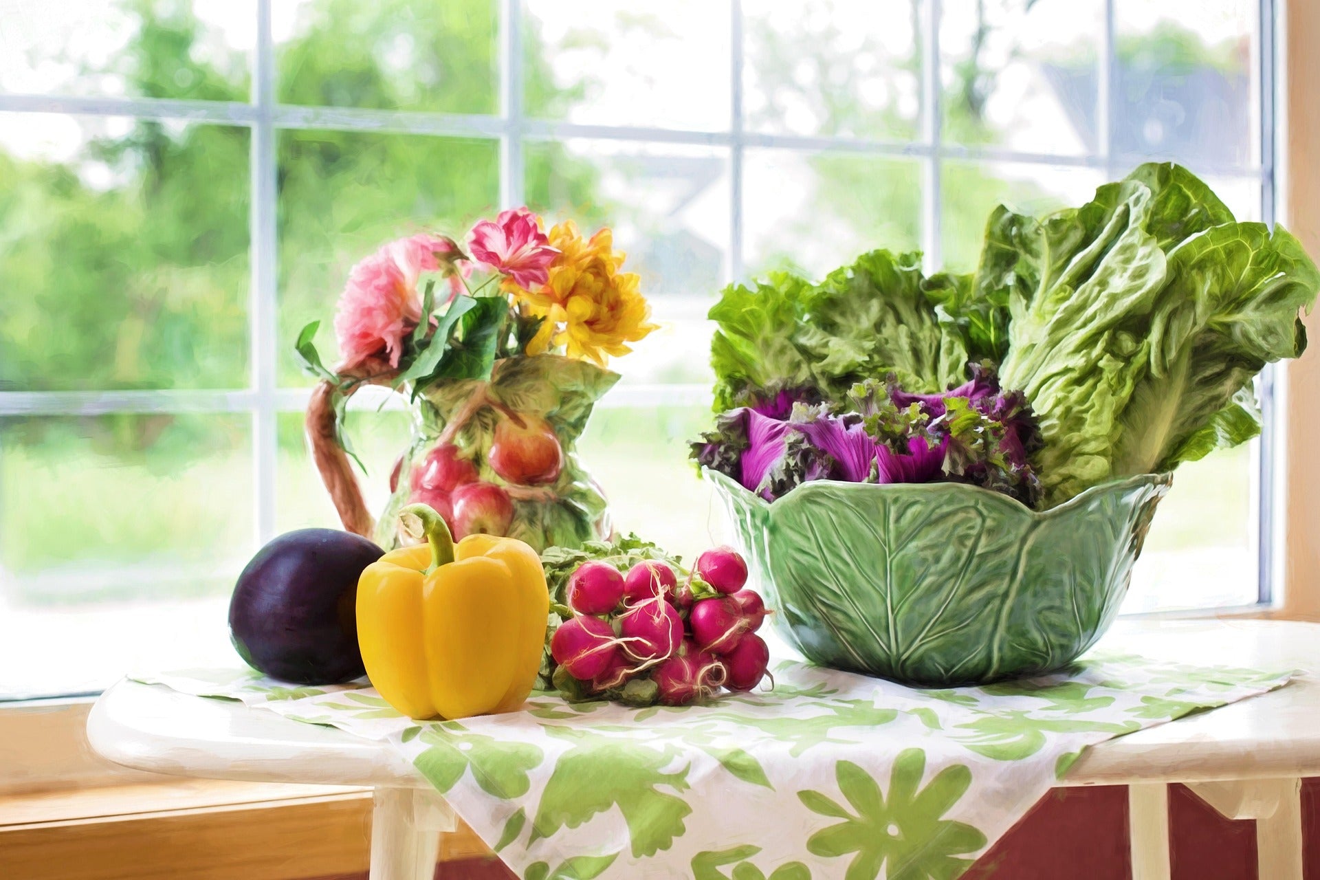 Assorted fresh vegetables and flowers on a table in front of a window.